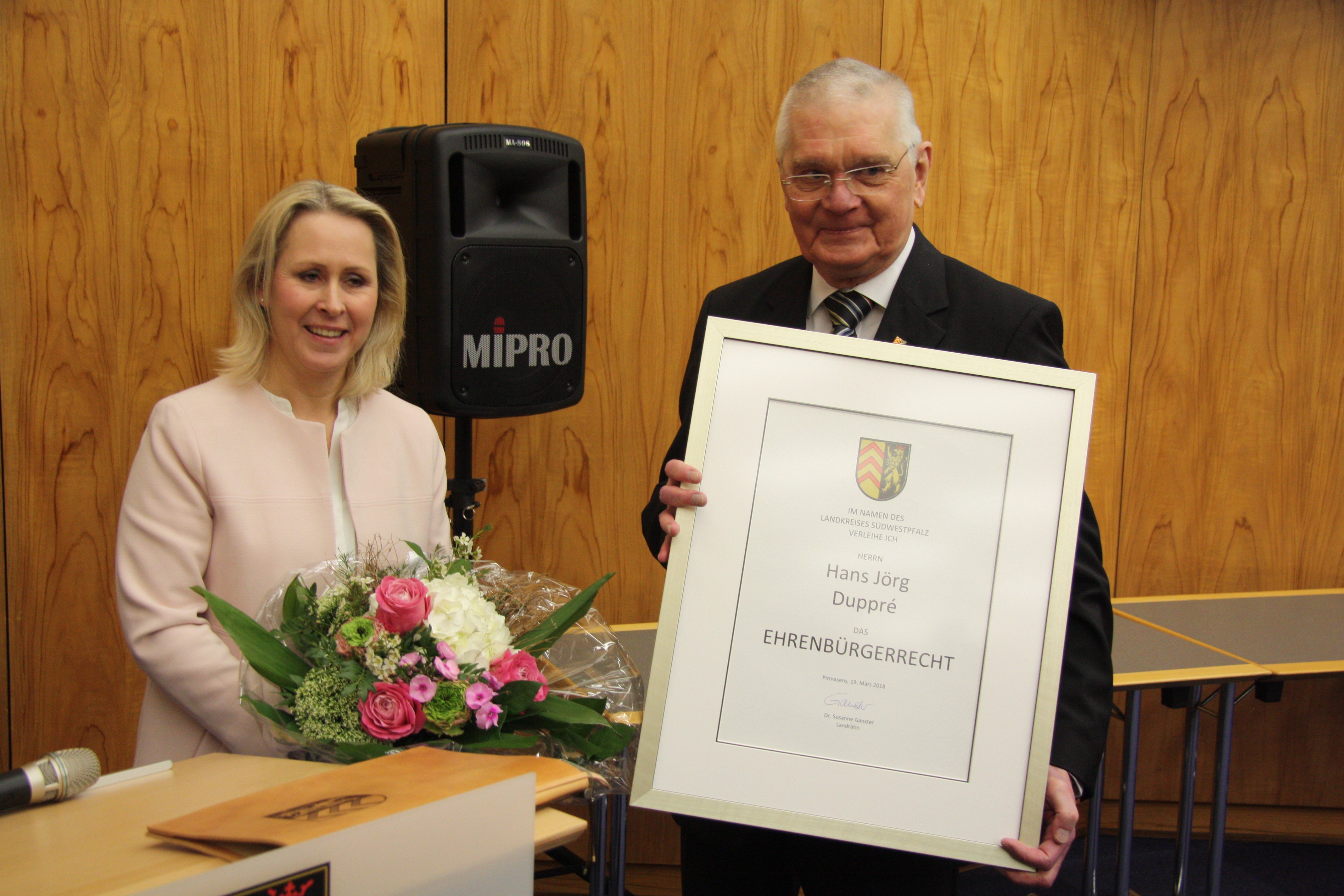 Landrätin Dr. Susanne Ganster mit Blumen in der Hand und der geehrte Hans Jörg Duppré mit einer gerahmten Urkunde