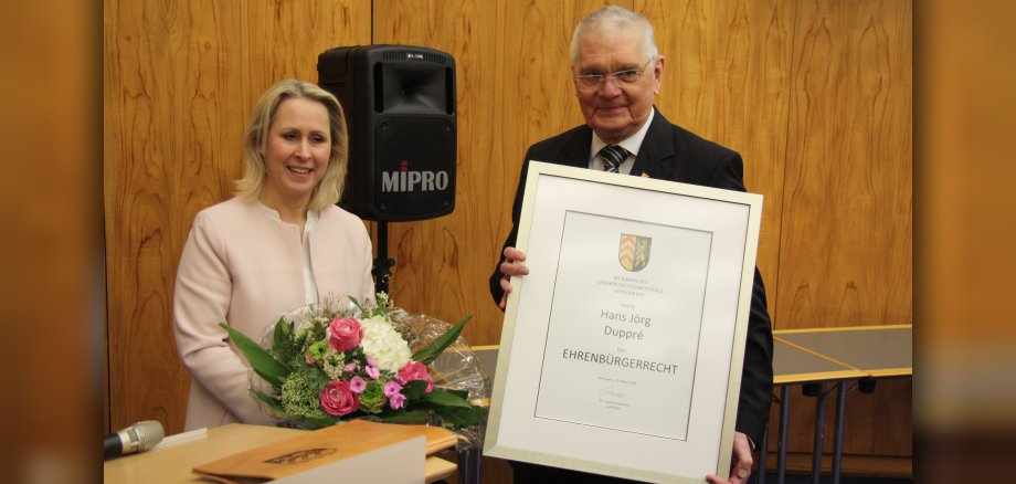 Landrätin Dr. Susanne Ganster mit Blumen in der Hand und der geehrte Hans Jörg Duppré mit einer gerahmten Urkunde